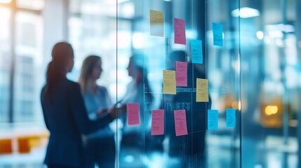 Business colleagues engage in a discussion, referencing sticky notes on a glass wall in a bright and modern office