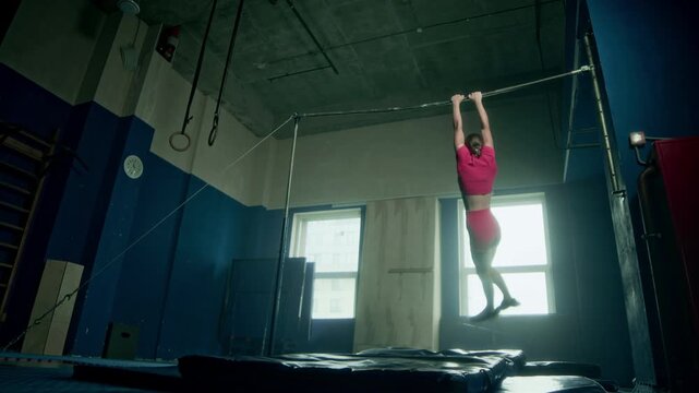 Slowmo of skilled Caucasian gymnast girl in pink sportswear making flip from bar and landing perfectly on mat while training at loft style studio