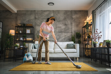 Mature japanese woman vacuums carpet with a vacuum cleaner at home