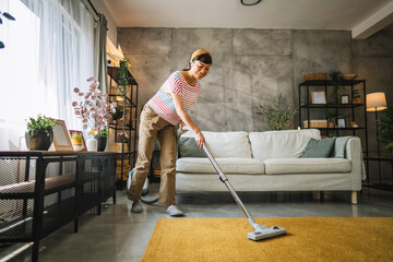 Mature japanese woman vacuums carpet with a vacuum cleaner at home