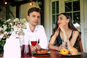 Happy Valentine's day, anniversary, and birthday. Couple sharing a joyful moment while enjoying pastries and drinking red wine in a cozy outdoor café. Man and woman sitting closely in restaurant