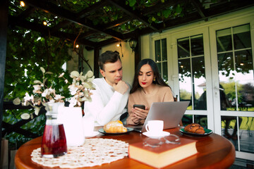 A joyful couple sharing a moment at a cozy café while browsing their phones and enjoying pastries in the bright afternoon light