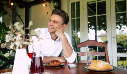 Man enjoying breakfast on a cozy patio with pastries, a drink, and greenery in the background during the morning