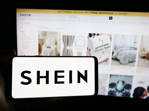 Stuttgart, Germany - 08-16-2024: Person holding smartphone with logo of fashion e-commerce company Shein in front of website. Focus on phone display.