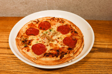 close up of freshly baked pizza or flatbread with salami, cheese, prawns and mayonnaise as toppings on a white plate on a wood table that look crispy and golden