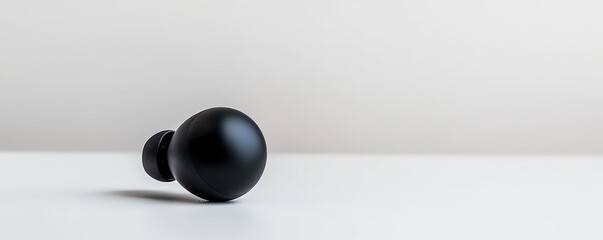 A minimalist black earbud resting on a clean surface, highlighting its sleek design and modern technology.