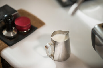 Metal jug with frothed milk to make a cappuccino.
