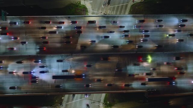 An aerial photo taken at night captures a crowded traffic jam in downtown Los Angeles. The freeway lanes are full of cars under the city lights, showcasing the bustling urban setting. Time lapse in 4K