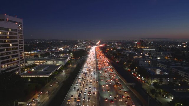 Aerial view of a traffic jam in Downtown Los Angeles, with city lights in the background. Cars are moving slowly on the roads in the evening, showcasing the heavy congestion in the area