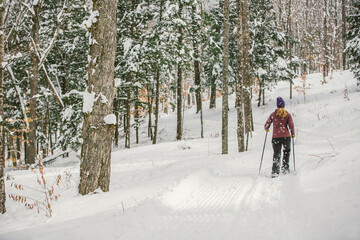 Woman snowshoeing in fresh snow in winter in the woods with blonde hair and purple coat in the cold.