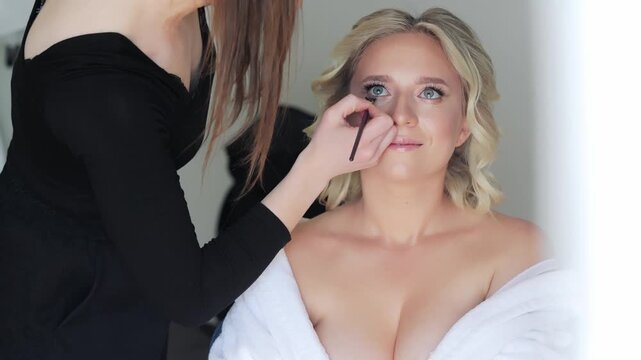 Bride Getting Ready with Makeup Artist's Touch, A candid shot of a bride getting her makeup done by a professional makeup artist.