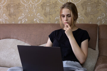 Young woman is deeply and thoughtfully engaging with her laptop in cozy, warm, and inviting home...