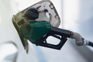 White car refueling at gas station with green fuel nozzle.