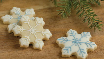 Three Snowflake Cookies with Cream, White and Blue Frosting on a Wood Surface