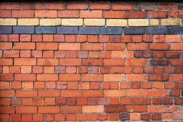 Obraz premium Weathered brick wall with a mix of red, yellow, and black bricks creating a textured and rustic appearance.