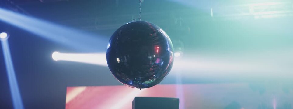 Silver mirror disco ball suspended from the ceiling rotates quickly, light spot rays and glare. White stage light at a concert hall, club, party or disco