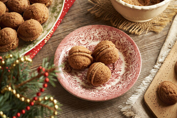 Three homemade Christmas cookies in the form of nuts filled with cream on a vintage plate with spruce tree branches