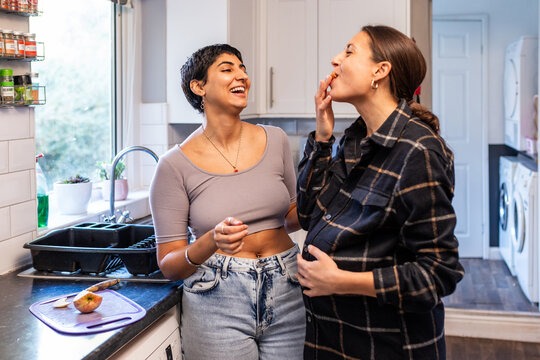 Lesbian couple sharing food and laughing in kitchen