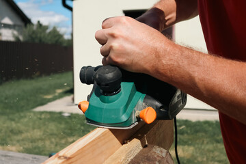 A carpenter planes a piece of wood using an electric plane. Carpenter is planing a wooden plank