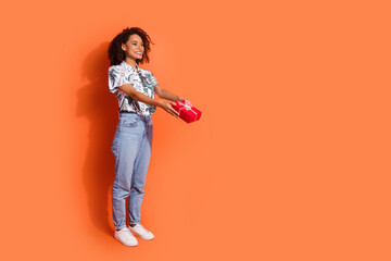 Photo of young beautiful happy girl curly hairstyle holding birthday box looking and giving surprise isolated on orange color background