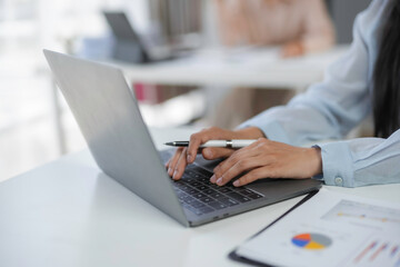 Businesswoman typing on laptop keyboard and holding pen in hand, working with financial data on white desk in modern office