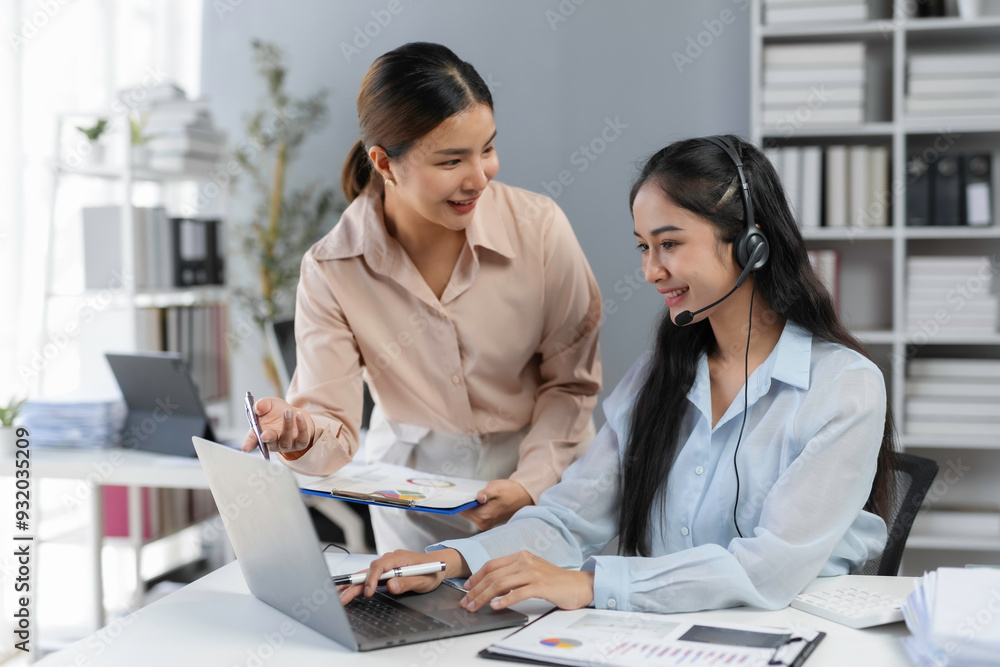 Poster manager is giving instructions to a smiling customer service operator who is working on a laptop