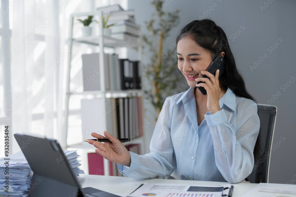 Poster smiling businesswoman having a phone conversation and pointing at a tablet while working in an offic