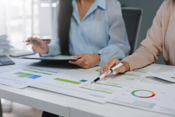 Businesswomen analyzing financial data and pointing at charts on a desk in the office