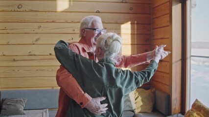 Medium shot of elderly Caucasian husband and wife dancing together in living room at home, swirling around, enjoying retro music, swaying to rhythm and chatting - Powered by Adobe