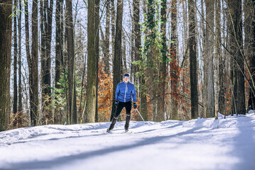 Man in blue jacket skiing through a snow-covered forest, enjoying a winter day outdoors surrounded...