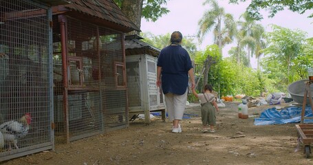 Asian Mother and Child Walking Through a Rural Farm with Chicken Coops and Lush Greenery on a sunny day. © HarryKiiM Stock