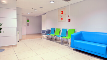 Modern waiting medical office area with white walls, a  tile floor and a row of armchairs.
