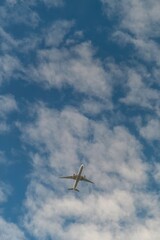 Commercial airplane flying high in the sky with scattered clouds on a sunny day