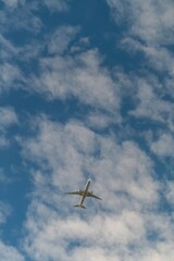 Commercial airplane flying high in the sky with scattered clouds on a sunny day