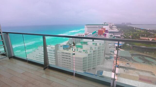 View from balcony with glass railing overlooking Caribbean large waves on rainy day with crashing onto sandy beaches of Mexican.