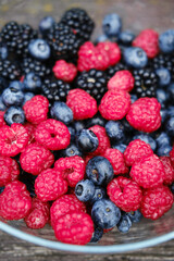 A glass plate full of summer berries on a wooden bench in the park. Fresh raspberries, blueberries and blueberries. A mix of healthy fruits.