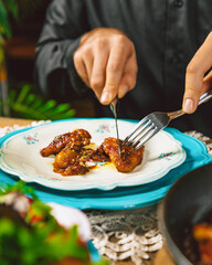 Man using cutlery eating chicken with barbecue sauce on a table