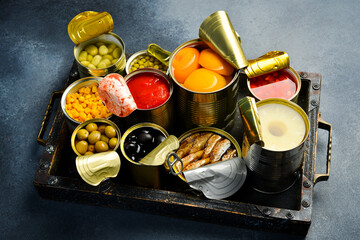 Canned vegetables, beans and fruits in tin cans on in a wooden box. Food stocks. Top view.