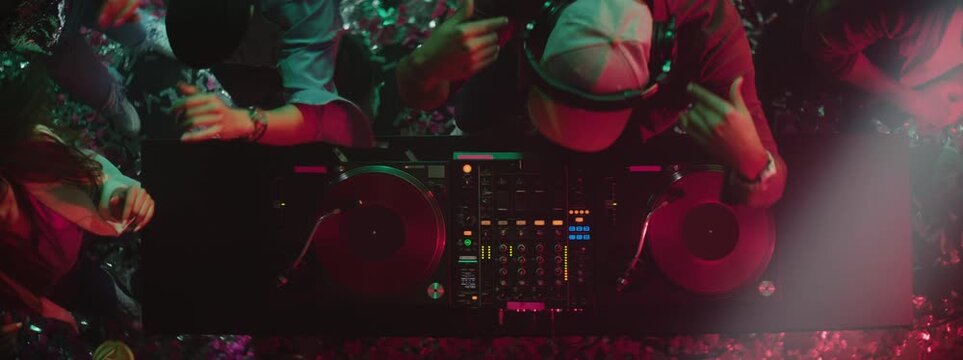 DJ turning jog wheel, moving slidder and switching the knob on dj mixer equipment controller while dancing with people around him