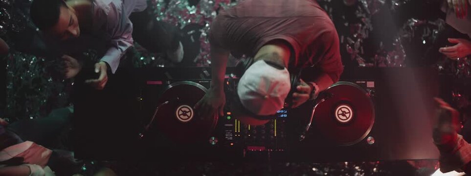 Top view of a male DJ playing music in club, attractive women dancing around in slow-motion. Nightlife, modern music and entertainment concept