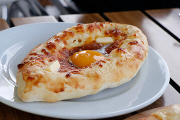 traditional Georgian bread with cheese, butter, egg known as adjaruli khachapuri plate in close up on table
