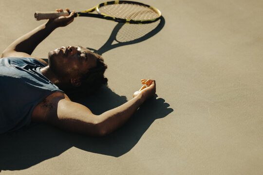 Exhausted tennis player laying down on court in sunlight