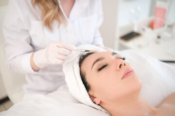 A cosmetologist girl makes injections on face of a beautiful girl in a beauty salon.
