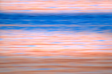 Obraz premium A motion blur applied to an ocean shore at sunset. The combination of beautiful blue and pale apricot horizontal lines invoke a sense of calm and serenity. Background for type and graphics.