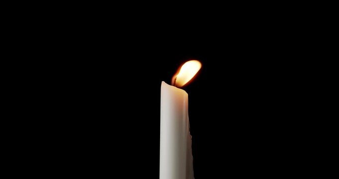 A single white candle burning. Isolated candle slow motion burning with dark background. White paraffin candle with yellow shades burns on a black background. Slow motion.