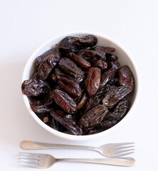 Dates in a bowl on a white background with two small forks next to them