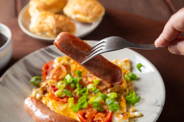Eggs with tomatoes and sausage in a plate on the table of coffee and a croissant of sausage