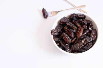 Dates inside a bowl on a white background with a dessert fork