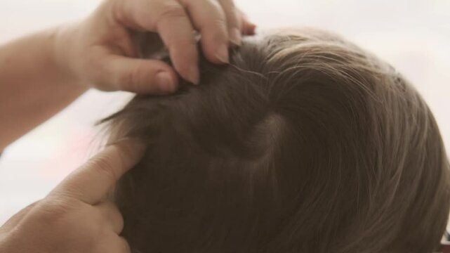 Close-up child's head with female hands searching for lice and nits in hair, regular hygiene and pest control, Pediculosis