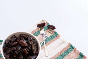 Bowl with portion of dried dates and forks with dates on top of a striped cloth